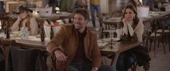 Movie still from “All the Places” (2023), directed by Pitipol Ybarra – A man sitting at a table with a glass of wine in front of him; Medium shot, Over the shoulder angle