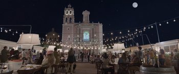 Movie still from “All the Places” (2023), directed by Pitipol Ybarra – People are sitting at tables in front of a building; Extreme Wide shot, Low angle