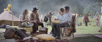 Movie still from “All the Places” (2023), directed by Pitipol Ybarra – A group of people sitting on a blanket in a field; Wide shot, Over the shoulder angle