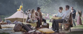 Movie still from “All the Places” (2023), directed by Pitipol Ybarra – A group of people sitting on the ground in a park; Wide shot, Over the shoulder angle