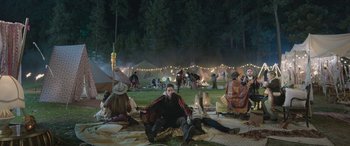 Movie still from “All the Places” (2023), directed by Pitipol Ybarra – A group of people sitting on the grass at night; Wide shot, High angle