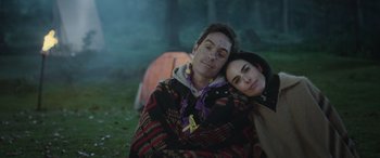 Movie still from “All the Places” (2023), directed by Pitipol Ybarra – A man and a woman sitting next to each other in the grass; Close Up shot, High angle