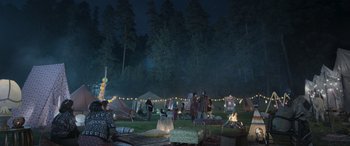 Movie still from “All the Places” (2023), directed by Pitipol Ybarra – A group of people sitting in a field at night; Extreme Wide shot, High angle