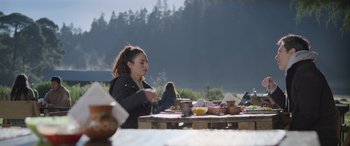Movie still from “All the Places” (2023), directed by Pitipol Ybarra – A woman sitting at a table with a plate of food in front of her; Wide shot, Over the shoulder angle