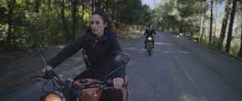 Movie still from “All the Places” (2023), directed by Pitipol Ybarra – Two people riding motorcycles down a road with trees in the background; Medium shot, High angle