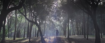 Movie still from “All the Places” (2023), directed by Pitipol Ybarra – Two people are walking through a forest on a foggy day; Extreme Wide shot, Low angle