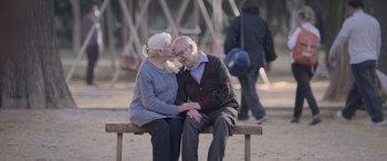 Movie still from “All the Places” (2023), directed by Pitipol Ybarra – An older man and woman sitting on top of a wooden bench; Wide shot, High angle