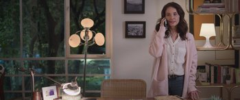 Movie still from “All the Places” (2023), directed by Pitipol Ybarra – A woman talking on a phone while standing in front of a table; Medium shot, Over the shoulder angle