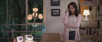 Movie still from “All the Places” (2023), directed by Pitipol Ybarra – A woman talking on a phone while standing at a table; Medium shot, High angle