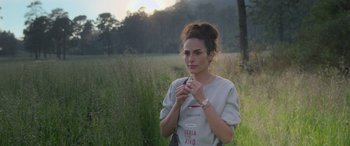 Movie still from “All the Places” (2023), directed by Pitipol Ybarra – A woman standing in a field holding something in her hand; Medium shot, Over the shoulder angle