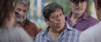 Movie still from “All the Places” (2023), directed by Pitipol Ybarra – A man with a beard and a blue and white checkered shirt; Close Up shot, Over the shoulder angle