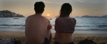 Movie still from “All the Places” (2023), directed by Pitipol Ybarra – A man and a woman sitting on the beach watching the sun go down; Medium shot, Low angle