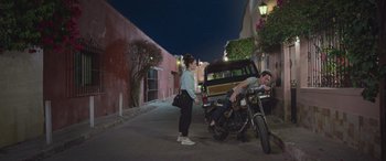 Movie still from “All the Places” (2023), directed by Pitipol Ybarra – A woman standing next to a man on a motorcycle; Wide shot, Low angle