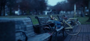 Movie still from “All Together Now” (2020), directed by Brett Haley – A person laying on a bench next to a bicycle; Wide shot, High angle