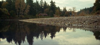 Movie still from “All Together Now” (2020), directed by Brett Haley – A person standing on a rocky shore next to a body of water; Extreme Wide shot, High angle
