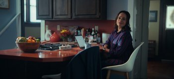 Movie still from “All Together Now” (2020), directed by Brett Haley – A woman sitting at a table with a laptop in front of her; Medium shot, Over the shoulder angle