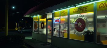 Movie still from “All Together Now” (2020), directed by Brett Haley – A store front with a neon sign and a doughnut shop; Extreme Wide shot, High angle