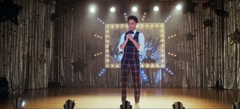 Movie still from “All Together Now” (2020), directed by Brett Haley – A man standing on a stage holding a microphone; Wide shot, Over the shoulder angle