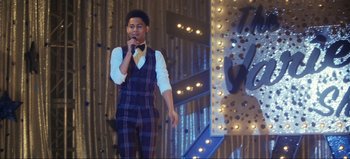 Movie still from “All Together Now” (2020), directed by Brett Haley – A man in a plaid suit is singing on a stage; Medium shot, Over the shoulder angle
