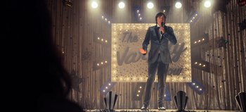 Movie still from “All Together Now” (2020), directed by Brett Haley – A man standing on a stage holding a microphone; Wide shot, Low angle