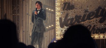 Movie still from “All Together Now” (2020), directed by Brett Haley – A man standing on a stage holding a microphone; Wide shot, Over the shoulder angle