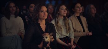 Movie still from “All Together Now” (2020), directed by Brett Haley – A woman holding a dog in her lap while sitting next to another woman in a crowd; Medium shot, High angle