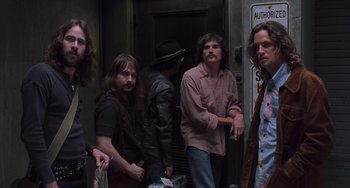 Movie still from “Almost Famous” (2000), directed by Cameron Crowe – A group of men standing next to each other in front of a door; Medium shot, Low angle