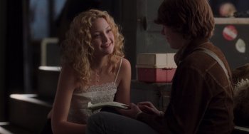 Movie still from “Almost Famous” (2000), directed by Cameron Crowe – A woman sitting next to a man holding a book; Medium shot, Over the shoulder angle