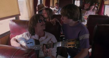 Movie still from “Almost Famous” (2000), directed by Cameron Crowe – A group of young people sitting on a couch playing guitars; Medium shot, Over the shoulder angle