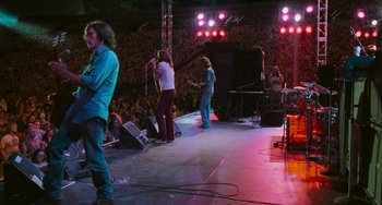 Movie still from “Almost Famous” (2000), directed by Cameron Crowe – A group of people standing on a stage with microphones; Wide shot, High angle