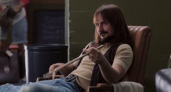 Movie still from “Almost Famous” (2000), directed by Cameron Crowe – A man sitting in a chair holding a stick; Medium shot, Low angle