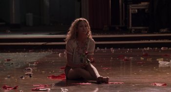 Movie still from “Almost Famous” (2000), directed by Cameron Crowe – A woman sitting on the ground holding a rose; Wide shot, High angle