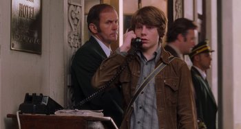 Movie still from “Almost Famous” (2000), directed by Cameron Crowe – A man talking on a phone next to another man in a suit; Medium shot, Over the shoulder angle