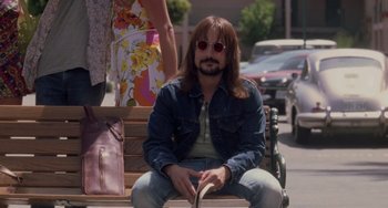 Movie still from “Almost Famous” (2000), directed by Cameron Crowe – A man sitting on a bench in the middle of the street; Medium shot, Low angle