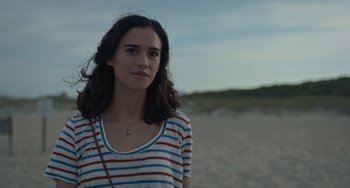 Movie still from “Along for the Ride” (2022), directed by Sofia Alvarez – A woman standing on the beach in a striped shirt; Close Up shot, Over the shoulder angle