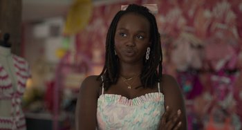 Movie still from “Along for the Ride” (2022), directed by Sofia Alvarez – A woman with dreads and a bow in her hair is posing for the camera; Close Up shot, Over the shoulder angle