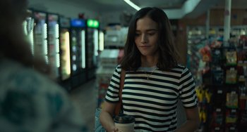Movie still from “Along for the Ride” (2022), directed by Sofia Alvarez – A woman holding a cup of coffee in a store; Medium shot, Over the shoulder angle
