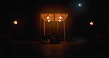 Movie still from “Along for the Ride” (2022), directed by Sofia Alvarez – Two people sitting on a bench at night under a canopy; Extreme Wide shot, Over the shoulder angle