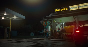 Movie still from “Along for the Ride” (2022), directed by Sofia Alvarez – A night time photo of a russell's donut shop; Extreme Wide shot, Low angle