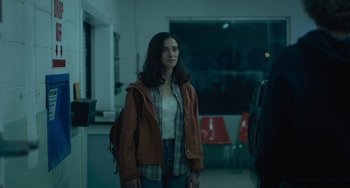 Movie still from “Along for the Ride” (2022), directed by Sofia Alvarez – A woman standing in a room with a backpack; Medium shot, Over the shoulder angle