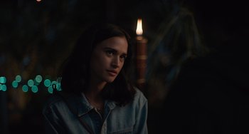 Movie still from “Along for the Ride” (2022), directed by Sofia Alvarez – A woman standing in front of a lit candle in the dark; Close Up shot, Over the shoulder angle