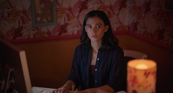 Movie still from “Along for the Ride” (2022), directed by Sofia Alvarez – A woman sitting at a table in front of a candle; Medium shot, High angle