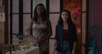 Movie still from “Along for the Ride” (2022), directed by Sofia Alvarez – Two women standing next to each other in front of a table; Medium shot, Low angle