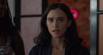 Movie still from “Along for the Ride” (2022), directed by Sofia Alvarez – A woman with long black hair wearing a blue and red shirt; Close Up shot, Over the shoulder angle