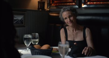 Movie still from “Along for the Ride” (2022), directed by Sofia Alvarez – An older woman sitting at a table with a glass of wine; Close Up shot, Over the shoulder angle