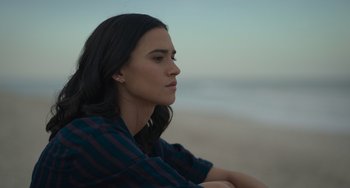 Movie still from “Along for the Ride” (2022), directed by Sofia Alvarez – A woman sitting on the beach looking into the distance; Close Up shot, High angle