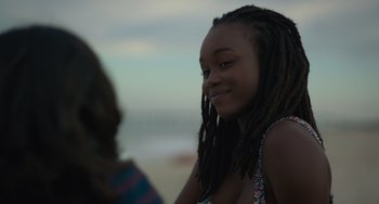 Movie still from “Along for the Ride” (2022), directed by Sofia Alvarez – A girl with dreads is smiling at the beach; Close Up shot, Over the shoulder angle