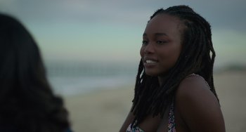 Movie still from “Along for the Ride” (2022), directed by Sofia Alvarez – A woman with dreads standing on the beach; Close Up shot, Over the shoulder angle