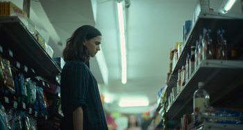 Movie still from “Along for the Ride” (2022), directed by Sofia Alvarez – A woman standing in front of a shelf in a store; Medium shot, Low angle