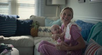 Movie still from “Along for the Ride” (2022), directed by Sofia Alvarez – A woman holding a baby in her arms and smiling; Medium shot, Over the shoulder angle